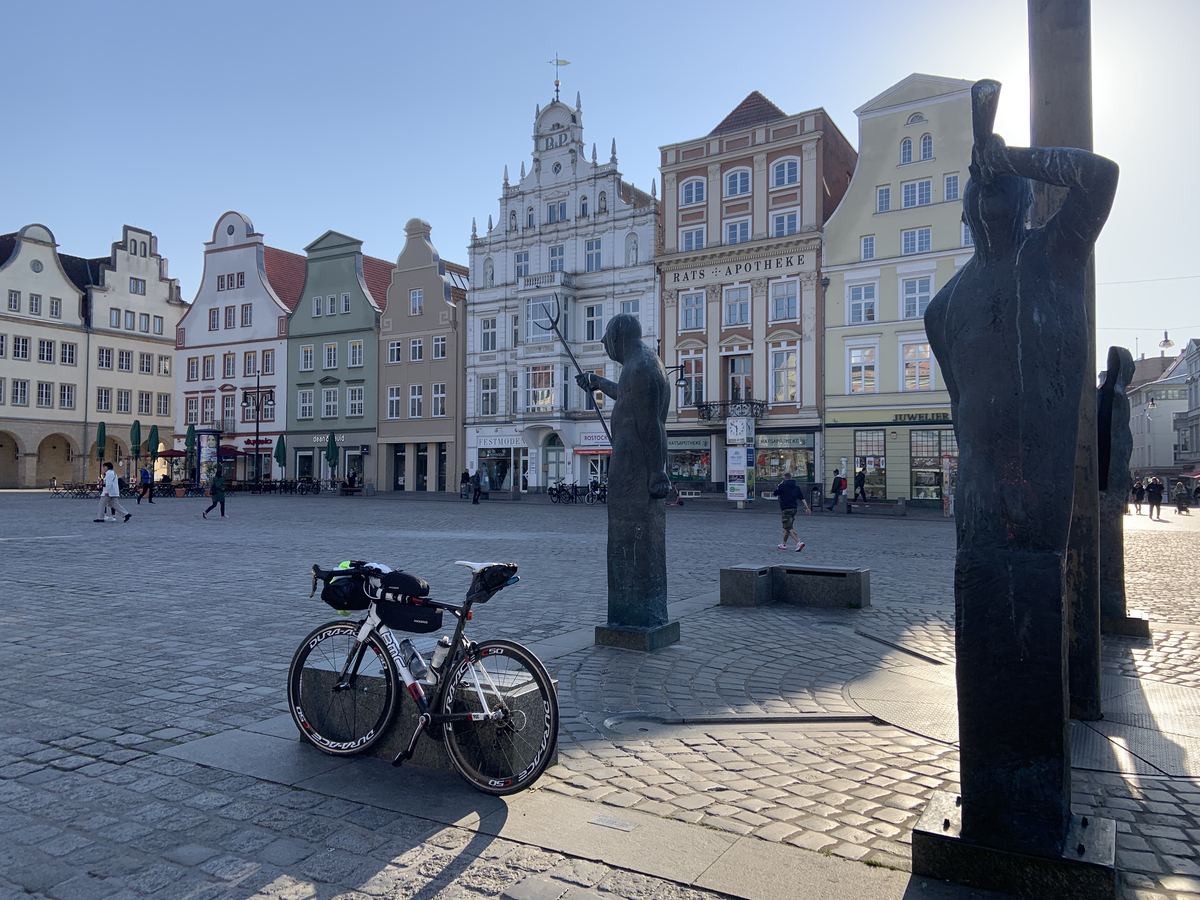 Neuer Markt in Rostock mit bunten Giebelhäusern, Bronzestatuen und Rennrad