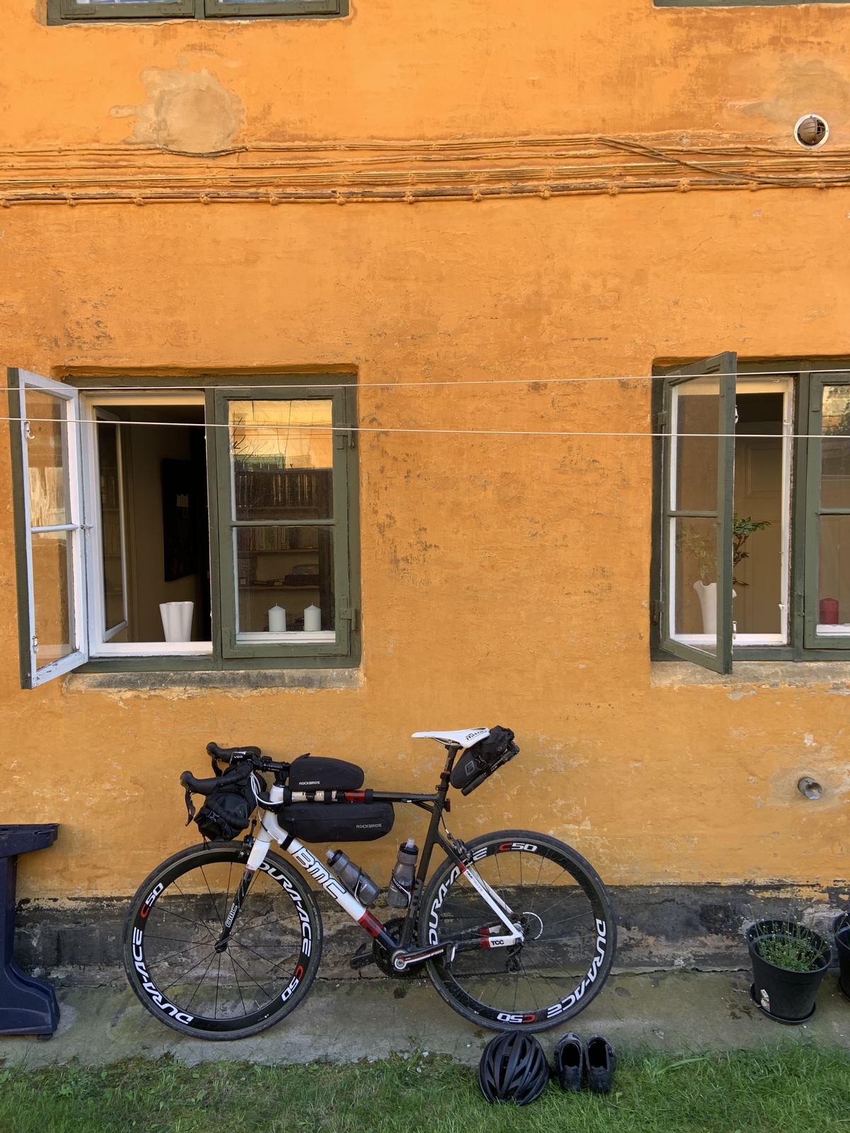 Rennrad vor einer ockerfarbenen Kopenhagener Hausfassade, Helm und Schuhe davor